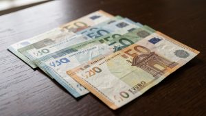 Billets en euros disposés sur une table en bois sombre, éclairés latéralement pour révéler leurs filigranes, reliefs et textures de sécurité.