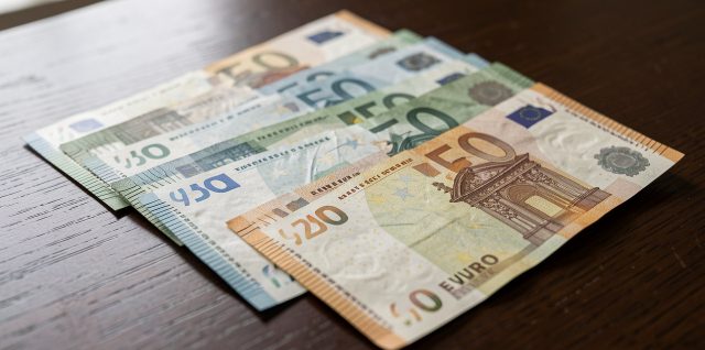 Billets en euros disposés sur une table en bois sombre, éclairés latéralement pour révéler leurs filigranes, reliefs et textures de sécurité.