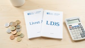 Deux livrets d’épargne français sobres, des pièces en euros et une calculatrice posés sur un bureau lumineux.
