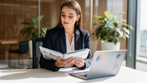 Une professionnelle examine un dossier de prévoyance et un tableau de charges abstrait sur un ordinateur dans un cabinet lumineux.